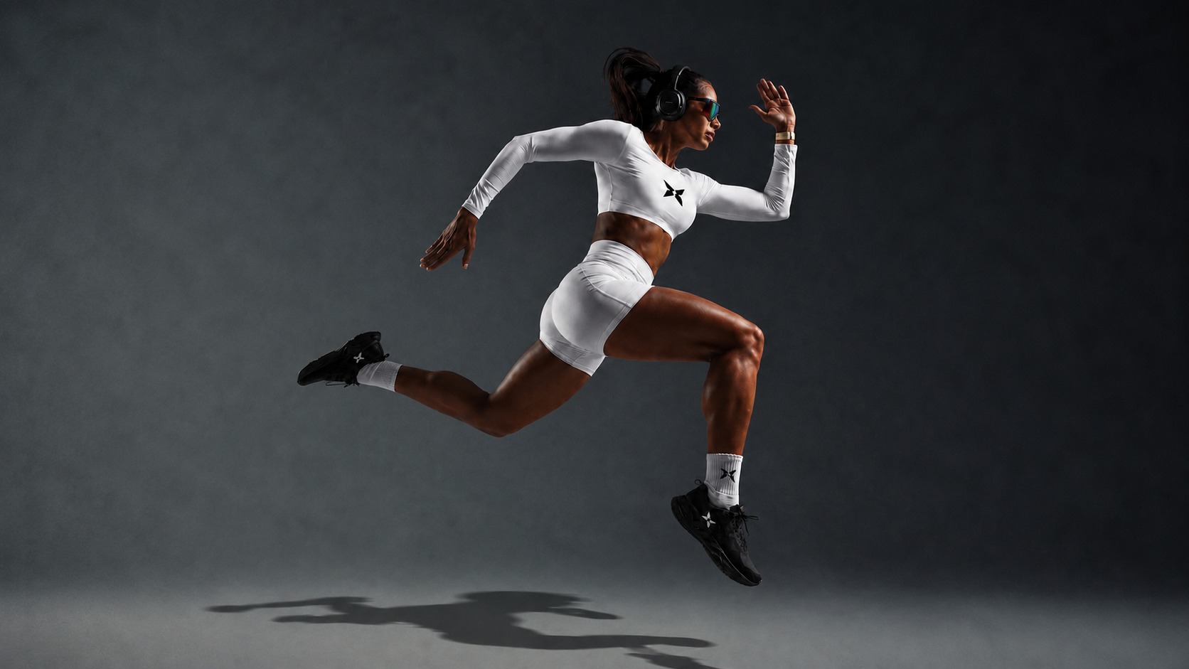 Athlete in mid-sprint wearing a white BRAVO long-sleeve crop and shorts, captured against a dark studio backdrop