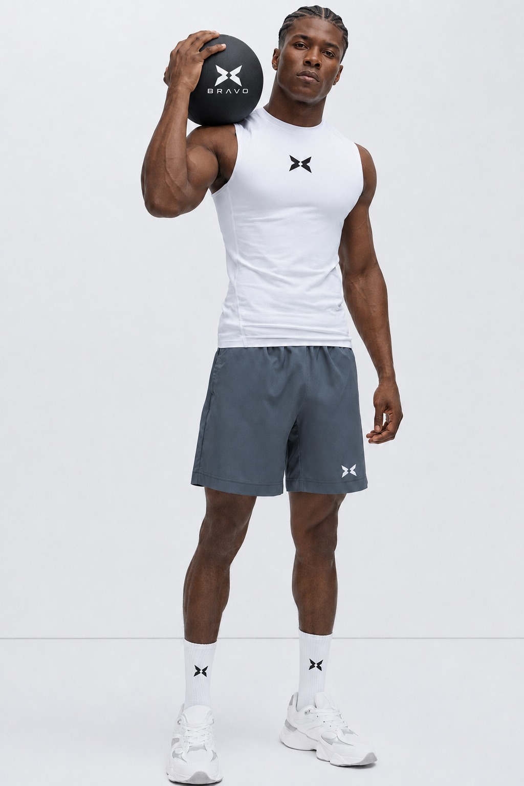 Man holding a BRAVO medicine ball wearing a white tank and charcoal shorts